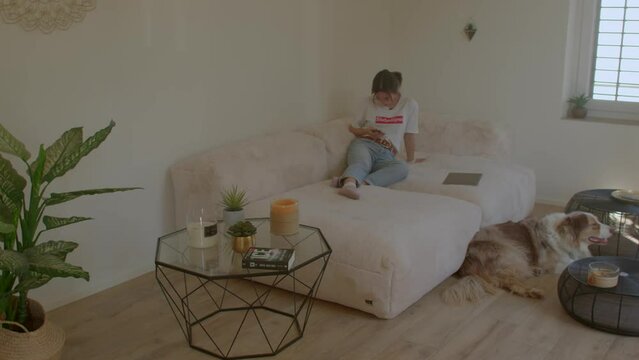 Girl with phone in her hands at couch in home interiors, the dog is lying on the floor. Internet addiction disorder (IAD) and procrastination, net addiction. CH, Zurich, 13.3.22