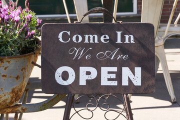 Sign in front of restaurant with text   Come In We Are Open. Dark coloured sign with white letters. Hospitality concept. 