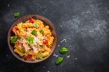 Italian pasta alla arrabiata with basil and parmesan on dark table. Fusilli pasta with tomato sauce. Top view, close up.