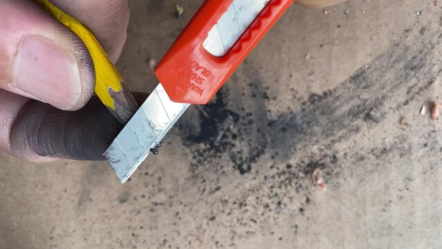Male hand artist sharpening pencil with a sharp blade box cutter knife close up shot, educational and carpentry concept with cardboard box background - day. Utility razor tool multi purpose uses
