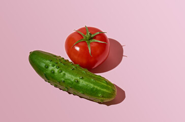 Tomato and cucumber with deep shadow isolated on a pink background. Close-up, top view, copy space.