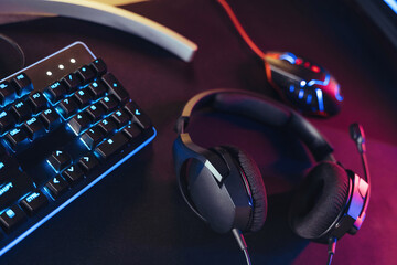 Close up of professional gaming setup on desktop in neon RGB colour. Mouse, keyboard, headset, monitor. Pro gamer's equipment is ready for online video games esport tournament and live streaming