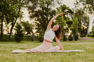 Young athletic woman practice yoga on gymnastic mat in green park on grass. Do do side bends and stretch muscles in sportswear, nature background. Concept of healthy lifestyle and harmony with body. © Юля Бурмистрова