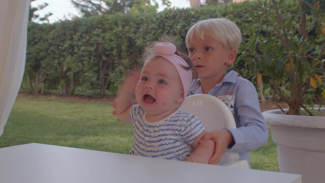 The boy tries to calm down his sister who needs attention. The child is screaming and nervous at the table. Helping older children to raise toddlers. IT, Borgagne, 6.10.2021 