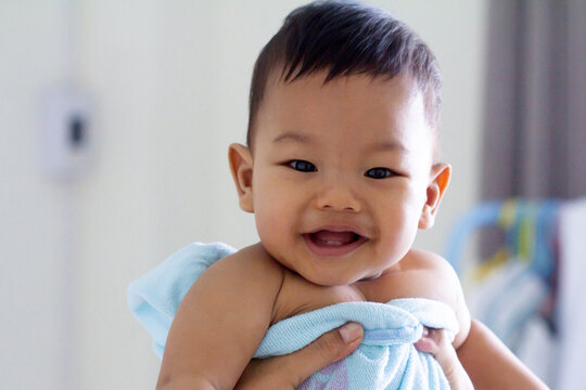 Mom hold his baby in the towel after bathing, Baby boy smiling and showing his two teeth. Indoors, close up with copy space
