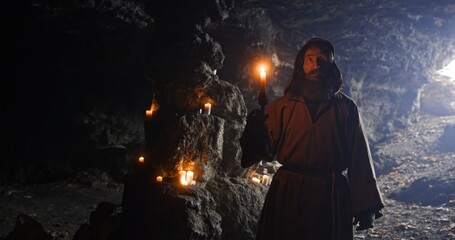 Elderly hermit with candle examining dark cave