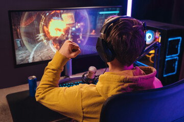 Back view of streamer young man rejoices his victory in esport shooter game tournament, making...