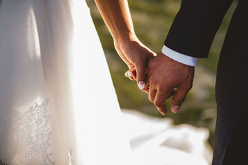 Closeup of the bride and groom holding hands in sunlight - obrazy, fototapety, plakaty