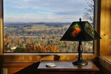 Lamp on a shelf by the window with the view of autumn landscape in the background