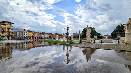 Naklejka premium Scenic view after strong rain on Prato della Valle, Abbey of Santa Giustina, square in city of Padua, Veneto, Italy, Europe. Rain storm and black clouds in sky. Water on street creates reflection