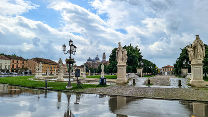 Scenic view after strong rain on Prato della Valle, Abbey of Santa Giustina, square in city of Padua, Veneto, Italy, Europe. Rain storm and black clouds in sky. Water on street creates reflection