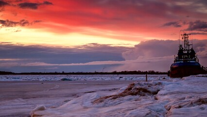 A frozen river with a tug near the shore against a bright dramatic sky at sunset.  beauty of nature