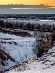 Fototapeta na wymiar Evening view of the ravine with a stream from melted snow at sunset. The coming of spring