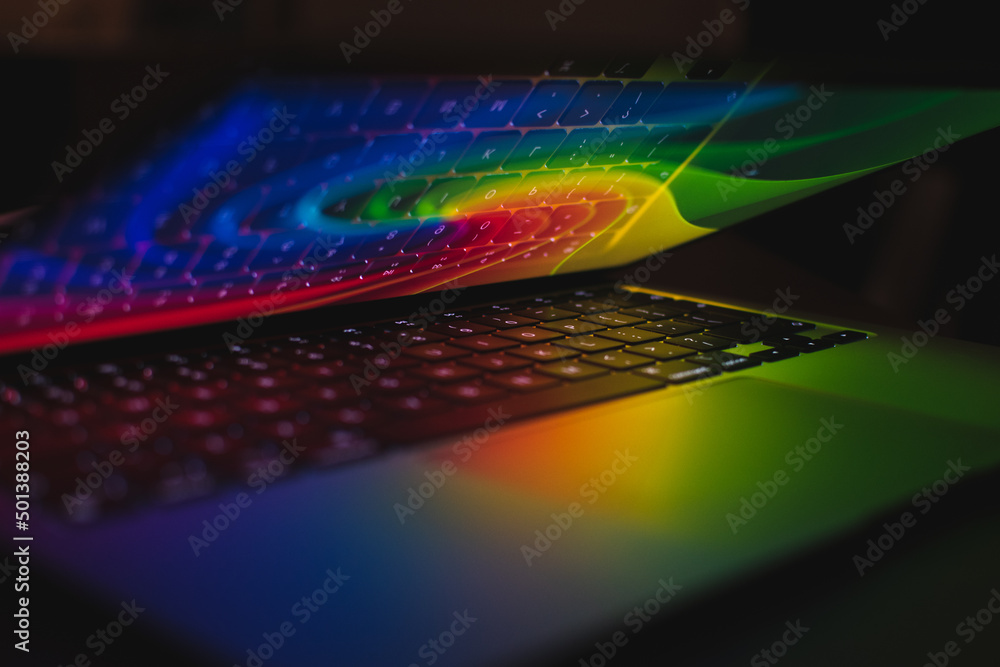 Poster closeup shot of an open laptop with rainbow light on it and a keyboard reflecting on a screen
