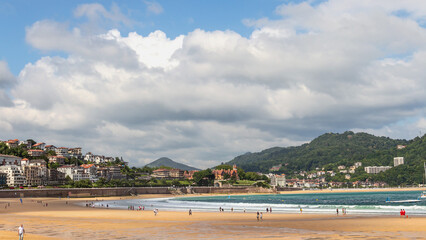 Obraz premium Wide sandy beach with people walking on a sunny day on the ocean coast in the Spanish city of San Sebastian