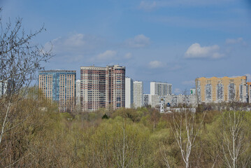 An urban residential area rises above a green park against a blue sky.