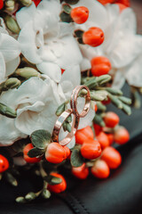 closeup wedding rings in wedding bouquet. two gold male and female rings on the bouquet flowers with red berries background. wedding details concept