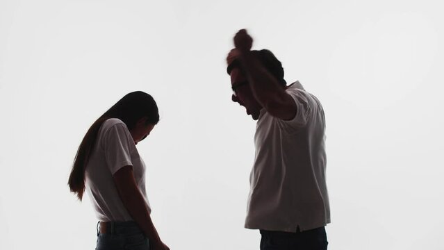 Silhouette of angry man who shakes hands and yells at woman, she guiltily lowered head, white background in studio, side view. Man yells at woman shaking hands over head