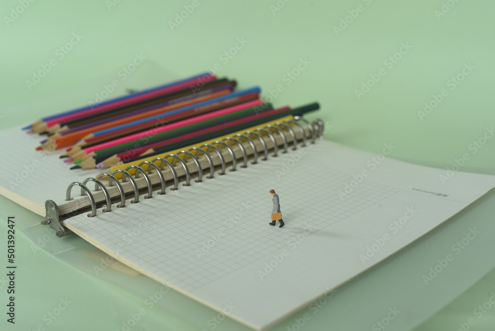 Aufkleber closeup shot of a notebook with colorful pencils and a statuette of a man on it-concept of knowledge
