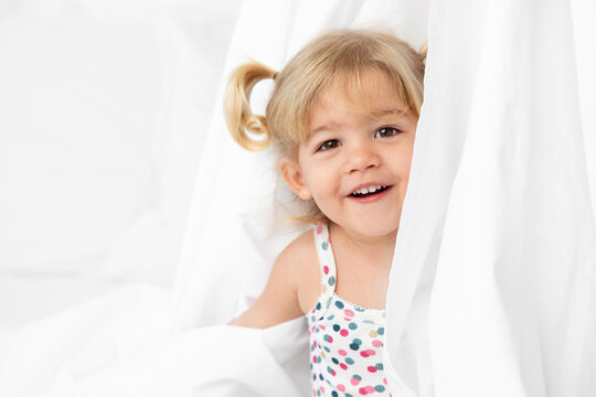 Happy toddler girl playing peekaboo behind white sheet