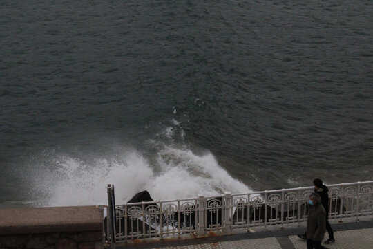 High angle view of two people walking by the pier near the water crashing on the rocks