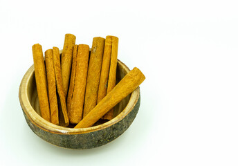 Cinnamon sticks in wooden bowl on white background with copy space