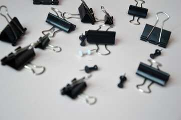 Black push pins and document clips and buttons scattered on a white background. Office tools.
