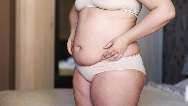 Close up of fat folds with big belly of overweight woman in underwear. Showing and using hands to squeeze fat belly. Excessive weight, obese female, overeating problems. Hiding and hold naked stomach