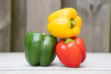 Green, yellow and red bell peppers on grey wooden background