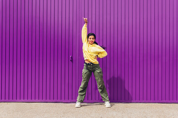 Full body of a young woman dancing outdoors with a purple background and yellow clothes. Concept of...