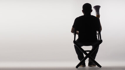 Silhouette of Back of Asian man sitting on black director chair. He holding a megaphone on white...