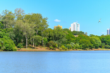 Landscape of Igapo lake, Londrina - PR, Brazil. Beautiful city lake, with trees around the shore, hiking trail and the city buildings on background.