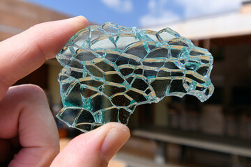 Holding on fingertips a broken piece of tempered glass, green tempered glass. Piece of glass with...