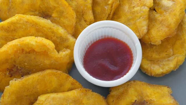 Fried platanos and sauce on plate. Sliced and cooked tostones. Rotating