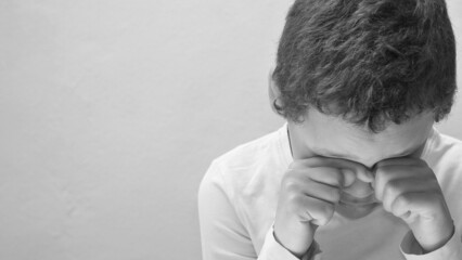 boy crying with hand over face crying alone and all by himself with white background