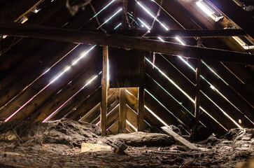 abandoned attic of an abandoned house, you can see wooden ceilings. Sunlight passes through cracks in the wall boards.