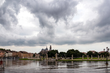 Fototapeta na wymiar Scenic view after strong rain on Prato della Valle, Abbey of Santa Giustina, square in city of Padua, Veneto, Italy, Europe. Rain storm, black clouds in sky. Isola Memmia surrounded by canal, statues