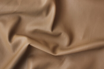 a piece of caramel beige artificial leather close-up with Abstract waves and folds of fabric