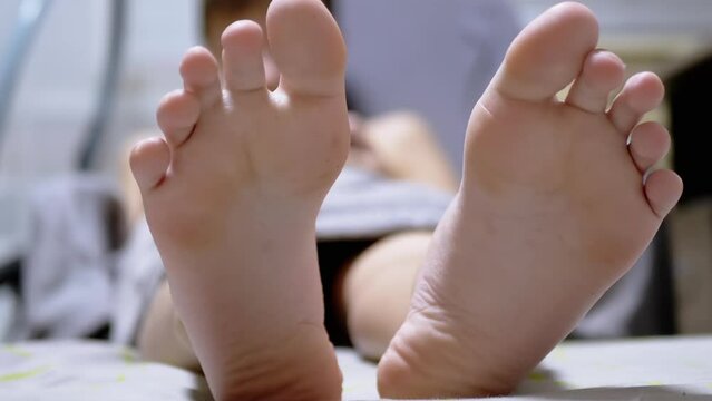 Close-up of Two Large Legs of a Sleeping Child on a Bed in a Room. The tired boy stretched out his long legs. Showing the toes, heels, feet of a falling asleep teenager. Resting, relaxing. Humor.