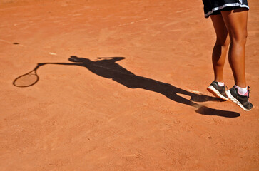 Legs and shadow of a female tennis player serving during on a clay court