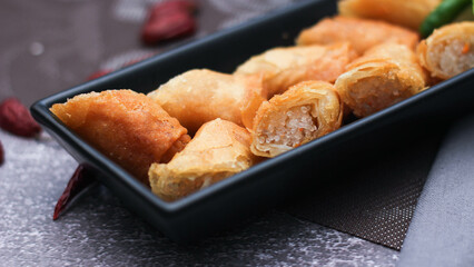 Fried spring rolls in a black plate served with tamarind dipping sauce on the table with black and gold placemats.