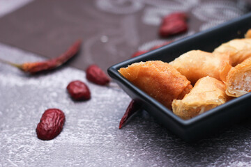 Fried spring rolls in a black plate served with tamarind dipping sauce on the table with black and gold placemats.