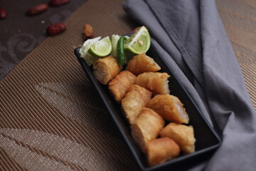 Fried spring rolls in a black plate served with tamarind sauce on a black wooden table
