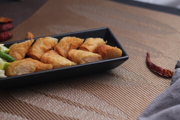Fried spring rolls in a black plate served with tamarind sauce on a black wooden table