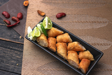 Fried spring rolls in a black plate served with tamarind sauce on a black wooden table