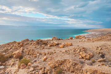 Dead sea shore at Jordan side, dry sand and rocks beach, sun shines on beautiful azure water surface