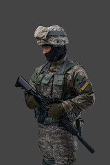 Portrait of soldier from ukraine with rifle dressed in uniform looking away isolated on gray background.