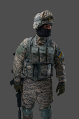 Portrait of soldier from ukraine with rifle dressed in uniform looking away isolated on gray background.