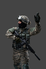 Portrait of attacking soldier equiped with modern uniform and weapon against gray background.