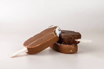 Chocolate ice cream bar with sticks. Melting and broken chocolate popsicles on pastel color background. Refreshing Summer dessert close up image.